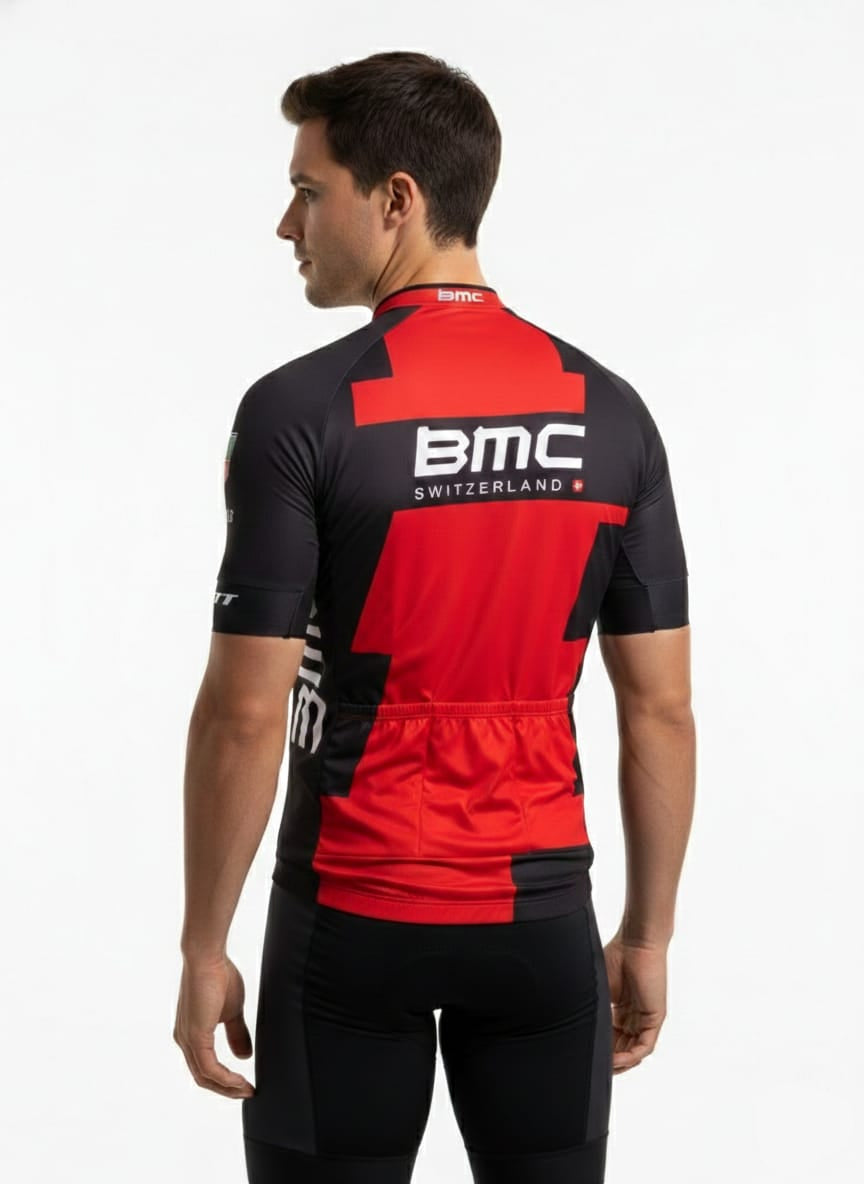 Cyclist standing on an open mountain road posing next to a BMC road bike, wearing the pro team red and black BMC Switzerland replica kit.