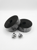 Two rolls of premium black bicycle handlebar tape secured in clear packaging alongside two metallic chrome handlebar end plugs on a white background