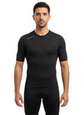 Front studio view of a male model wearing a tight-fitting, all-black Reeck short sleeve cycling jersey with a full-length zipper and a small white brand logo on the right shoulder.