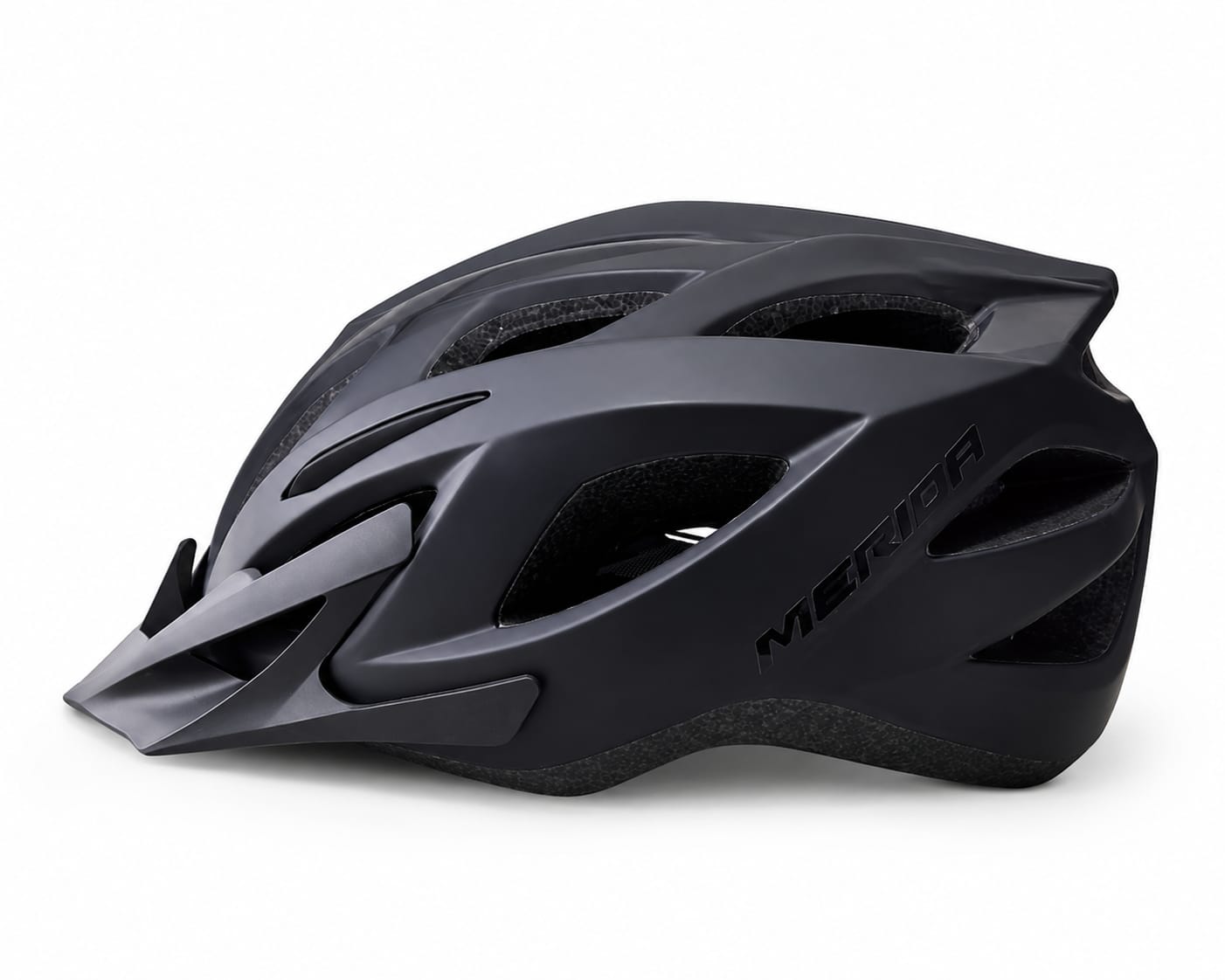 A side profile view of a MERIDA cycling helmet in a stealthy matte black colorway, featuring a matching removable front visor, tonal gloss black Merida branding on the side, and integrated ventilation channels in the black EPS foam liner, displayed against a clean white background