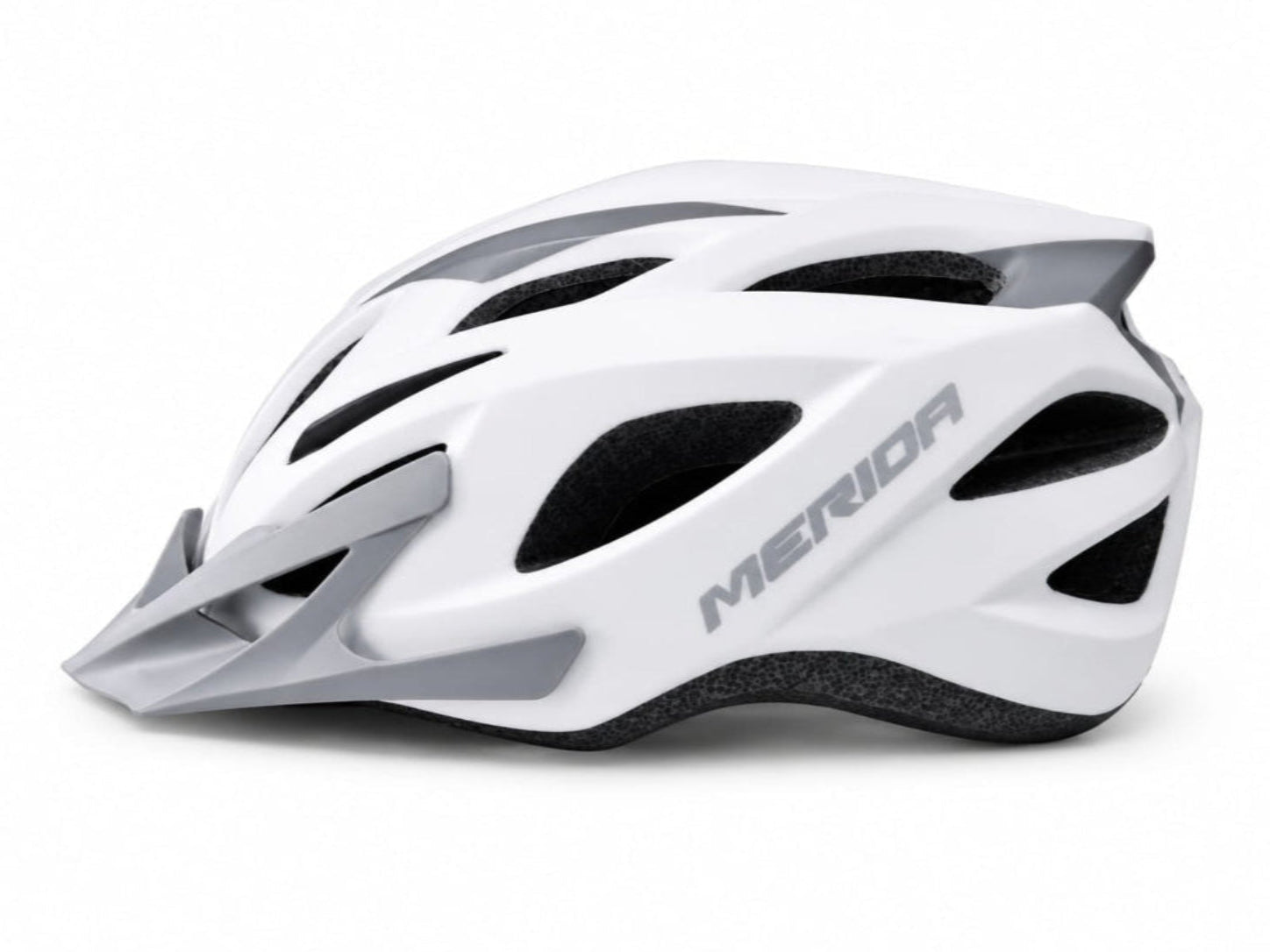 A side profile view of a MERIDA cycling helmet featuring a matte white outer shell with light grey structural accents and the Merida brand name printed on the side, including a matching removable grey visor and exposed black EPS foam ventilation channels, displayed against a white background