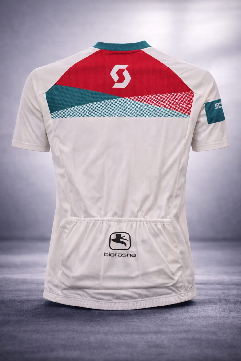 Back view of the off-white Scott cycling jersey showcasing the three elasticized rear storage pockets, a red shoulder yoke, and a lower back biorasna logo.