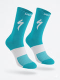 A pair of SPECIALIZED crew cycling socks in a vibrant turquoise teal colorway featuring a white midfoot compression band, a vertical white stripe down the back, and the iconic white lightning bolt logo on the upper cuff, displayed upright against a clean background