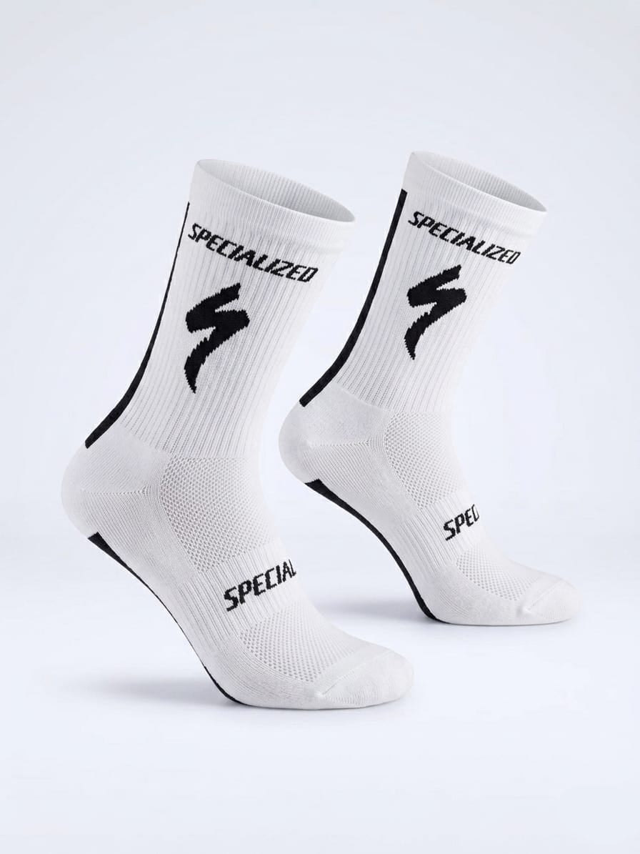 A pair of SPECIALIZED crew cycling socks in crisp white with a vertical black stripe down the back, featuring the iconic black lightning bolt logo and brand name on the upper ribbed cuff, displayed upright against a clean background.