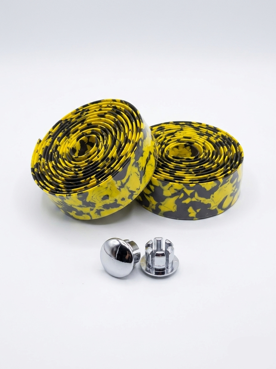Two rolls of premium yellow and black splatter patterned bicycle handlebar tape displayed together with two metallic chrome handlebar end plugs on a clean white background